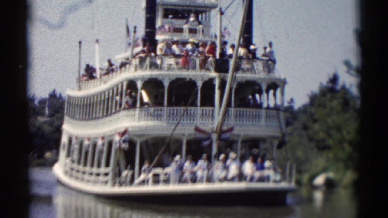 White riverboat with passengers on two decks moving along a calm waterway.