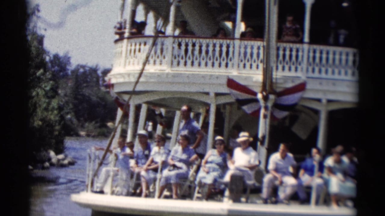 Visitors aboard a Disneyland riverboat sit along the lower deck as people look out from the upper balcony.