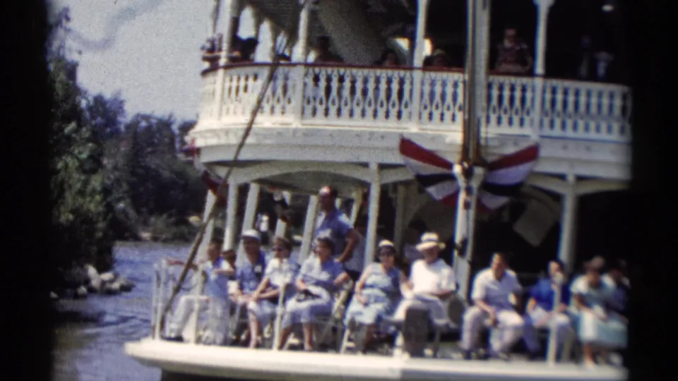Visitors aboard a Disneyland riverboat sit along the lower deck as people look out from the upper balcony.