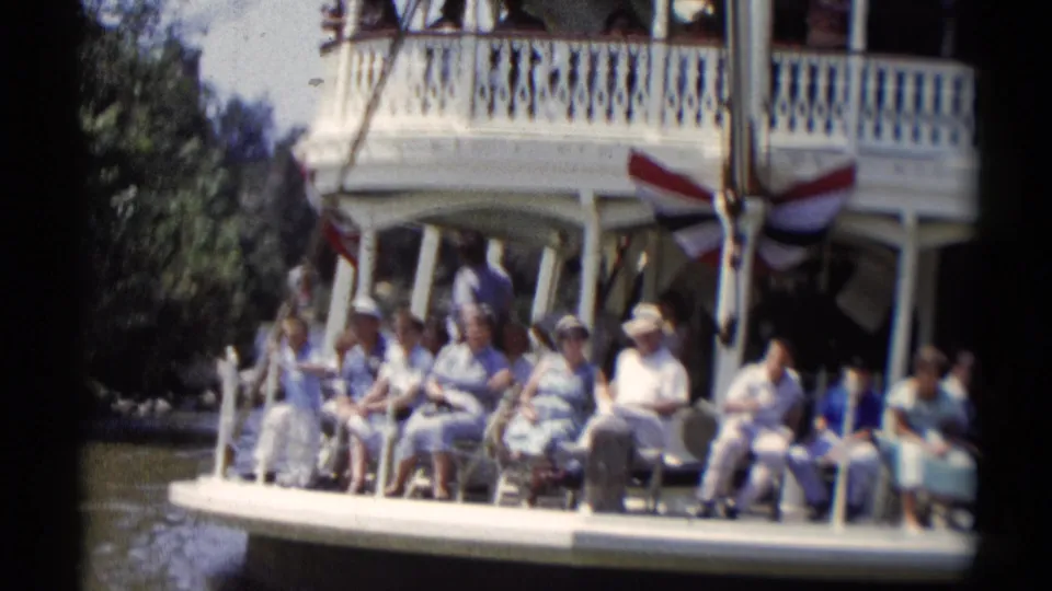 Disneyland riverboat passengers in light summer clothing sit beneath a decorated upper deck in 1959 footage.