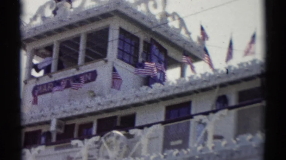 Handheld 1959 Disneyland view of the Mark Twain Riverboat, showing its sign, flags, upper-deck passengers, windows, and ornate trim.