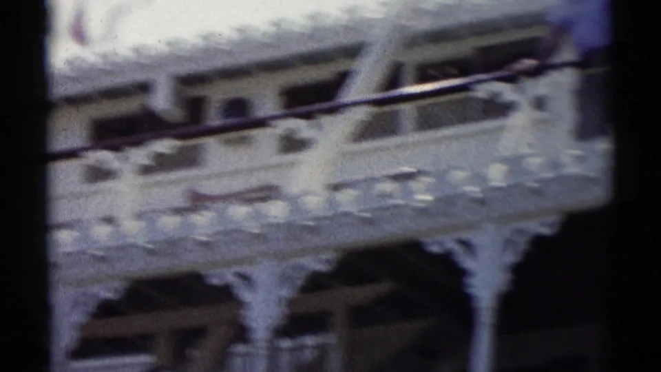 Soft 8mm Disneyland frame showing the Mark Twain Riverboat side, decorative white trim, windows, railing, and partial paddle-wheel structure.