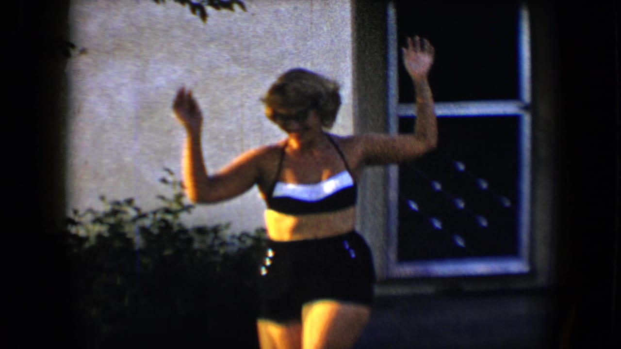 Young woman in a black and white swimsuit raises her arms on a sunny lawn near a window.