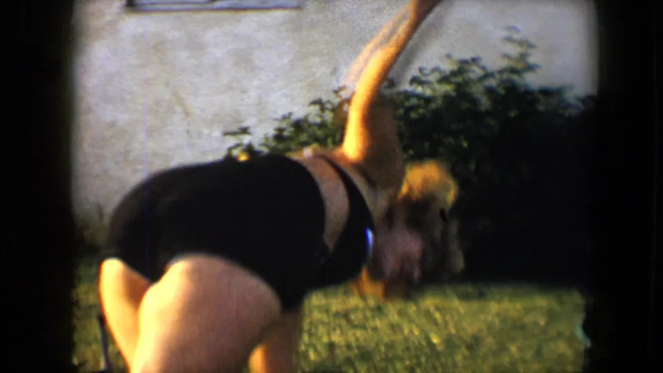 A young woman bends into a cartwheel on a sunlit backyard lawn, captured with soft 8mm color and dark frame edges.