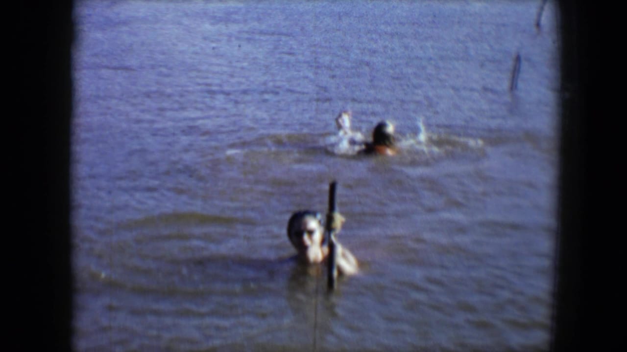 1959 Disneyland frame with one swimmer facing the camera near a post and another swimmer moving through the water behind.