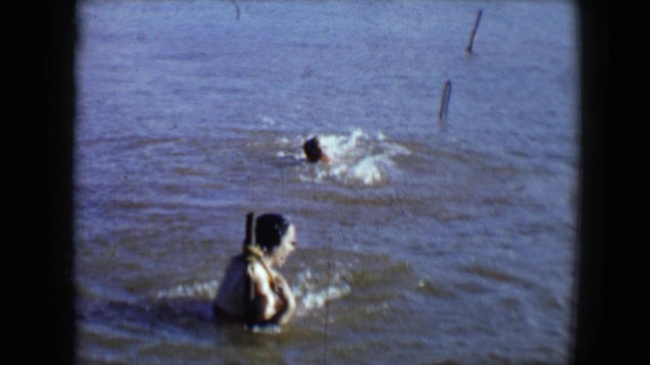 1959 Disneyland home-movie frame showing a woman in muddy water while another swimmer splashes in the background.
