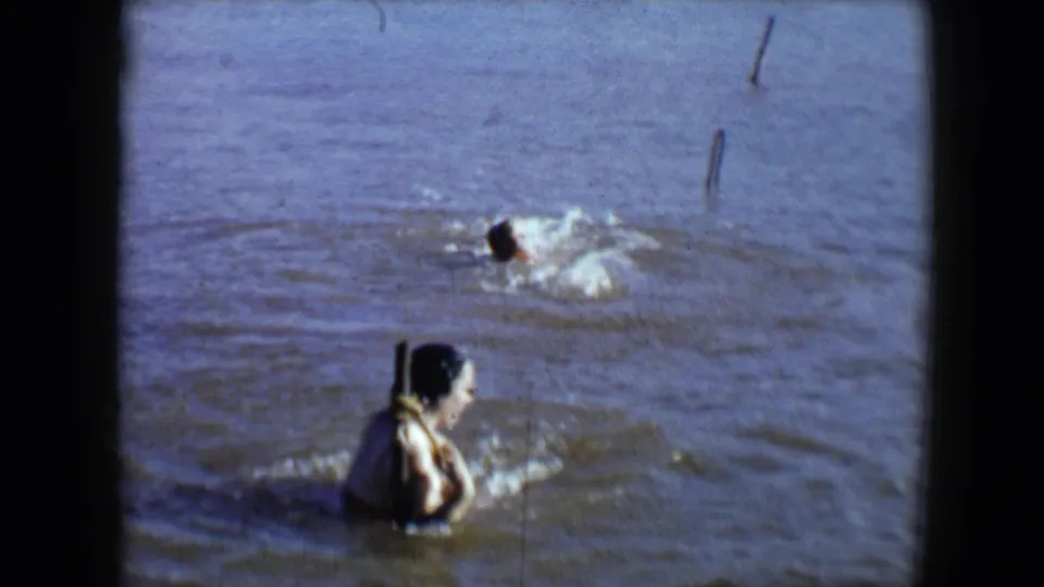 1959 Disneyland home-movie frame showing a woman in muddy water while another swimmer splashes in the background.