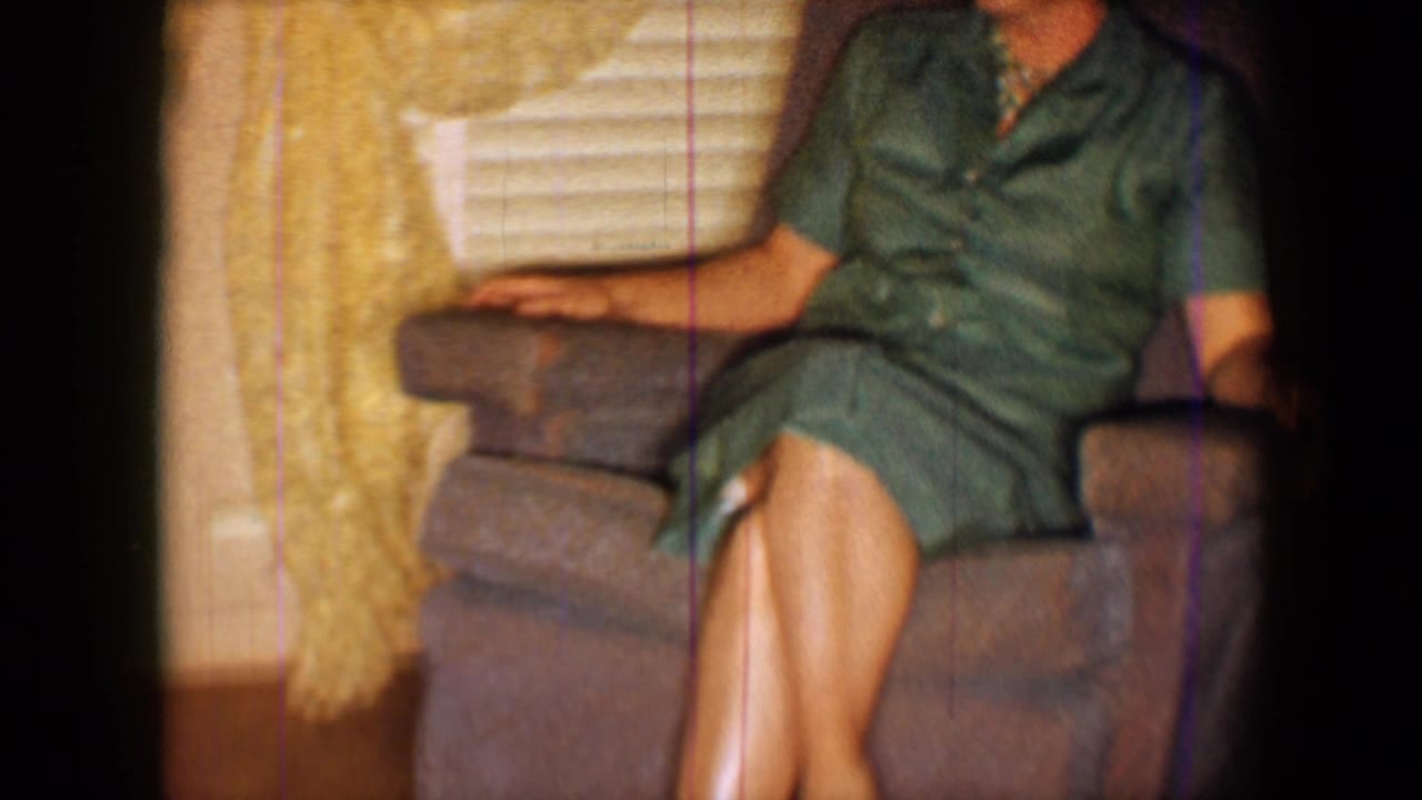 Seated woman in a green dress, cropped at the face, with crossed legs in a brown recliner.