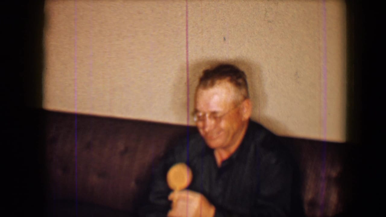 Man with glasses sits on a dark couch holding a round lolly.