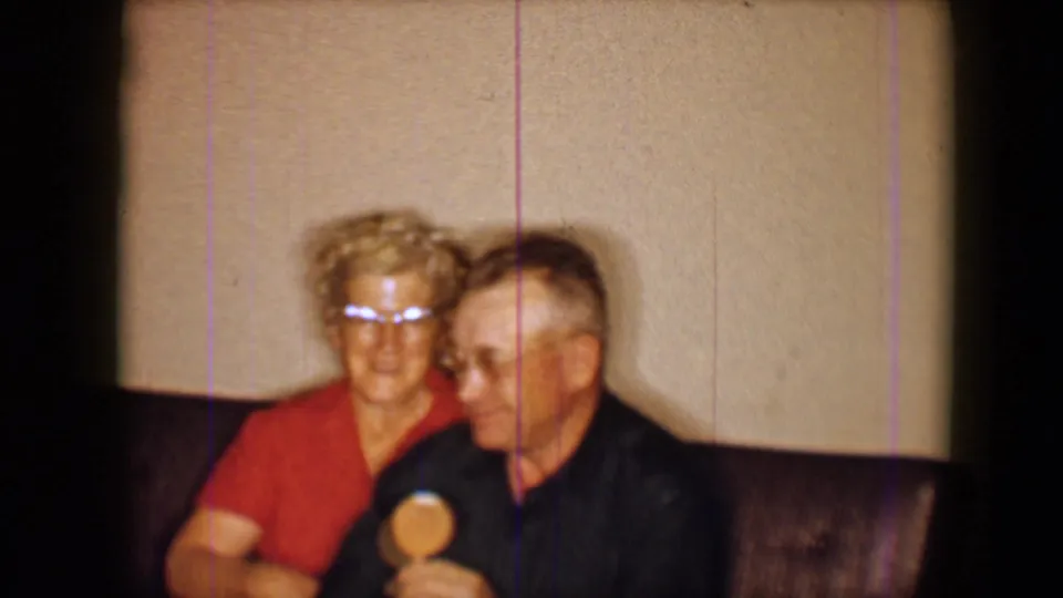 A woman in a red top and glasses sits close beside the man on the couch during the 1959 Disneyland home-movie moment.