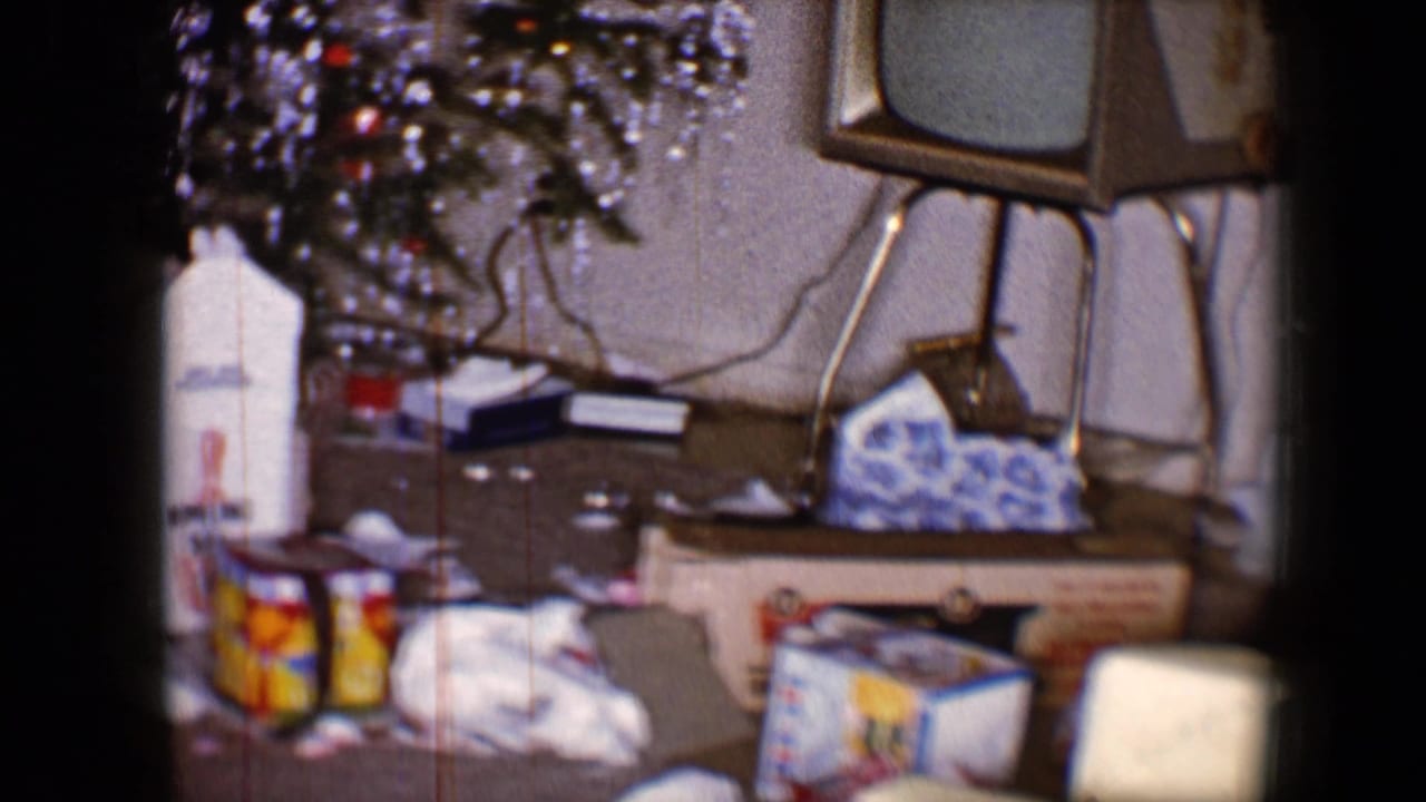 1959 8mm frame showing a decorated Christmas tree, scattered presents and a small television in a private living room.