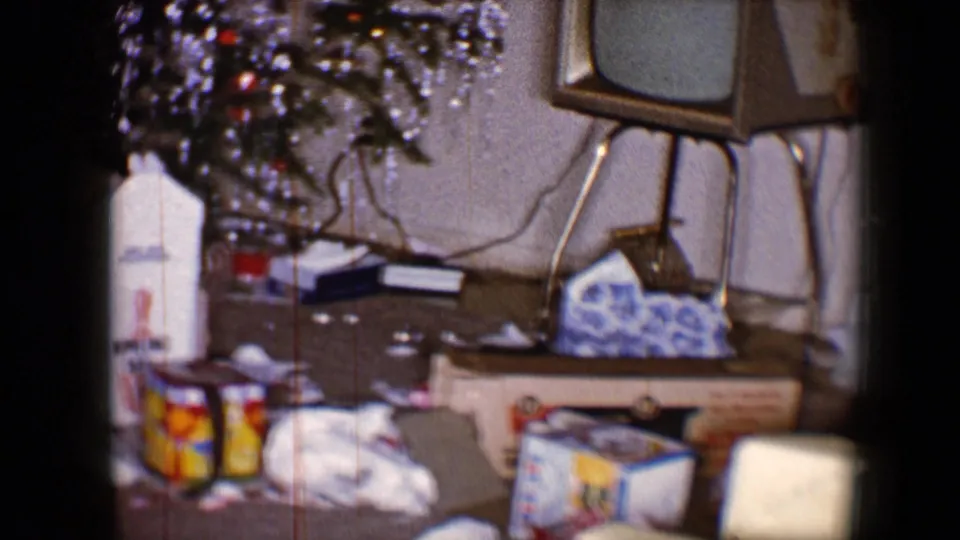 1959 8mm frame showing a decorated Christmas tree, scattered presents and a small television in a private living room.
