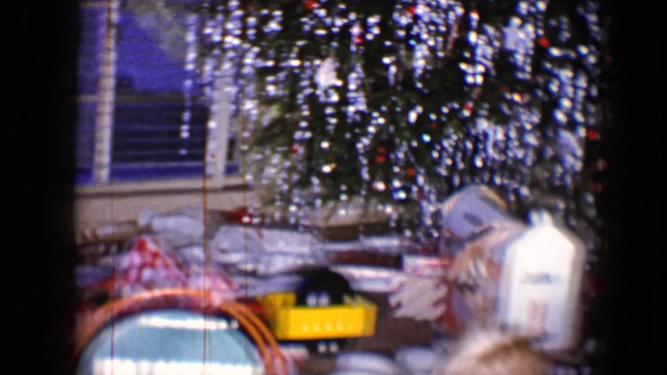 1959 8mm frame of a private holiday living room with a tinsel tree, window blinds, opened packages and gift wrap.