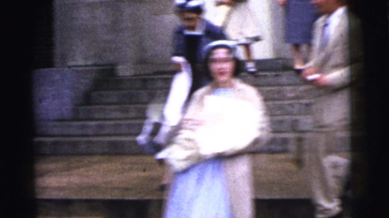 In Gary, Indiana, 1961, a woman in a light coat carries a swaddled newborn down exterior stone steps while adults gather around her.