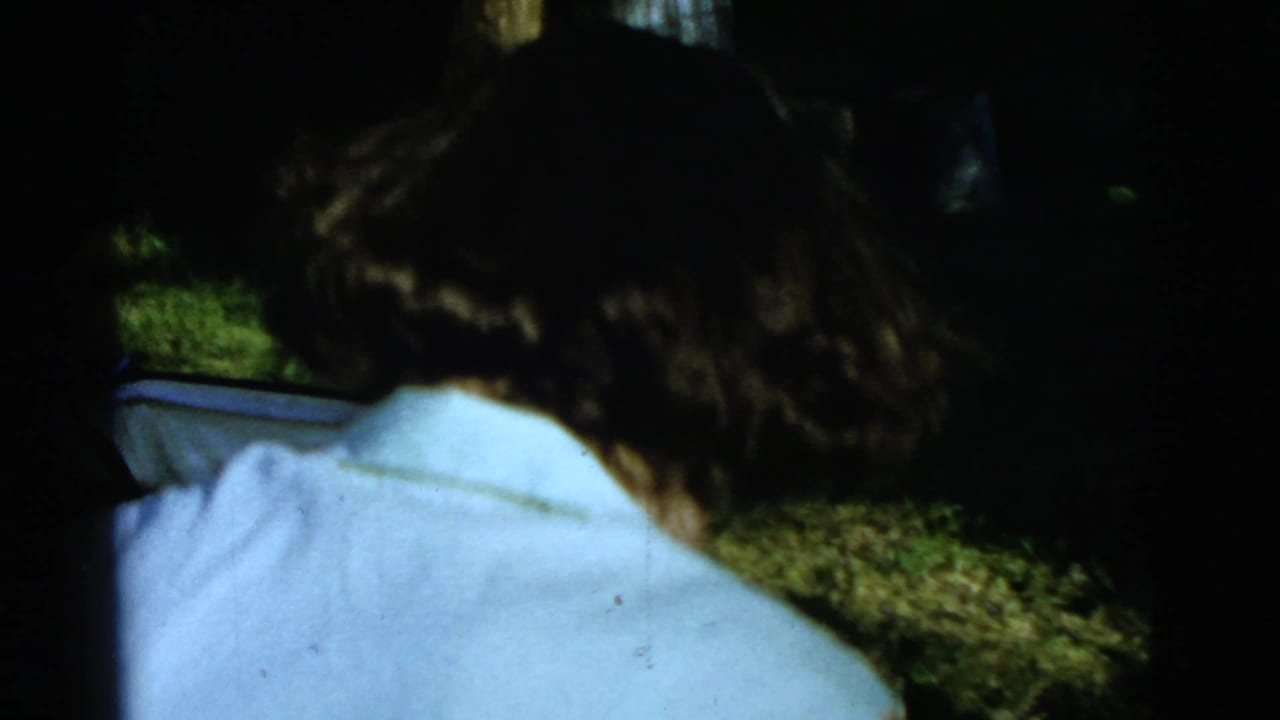 Woman seen from behind in a light blouse near grass and shadow.