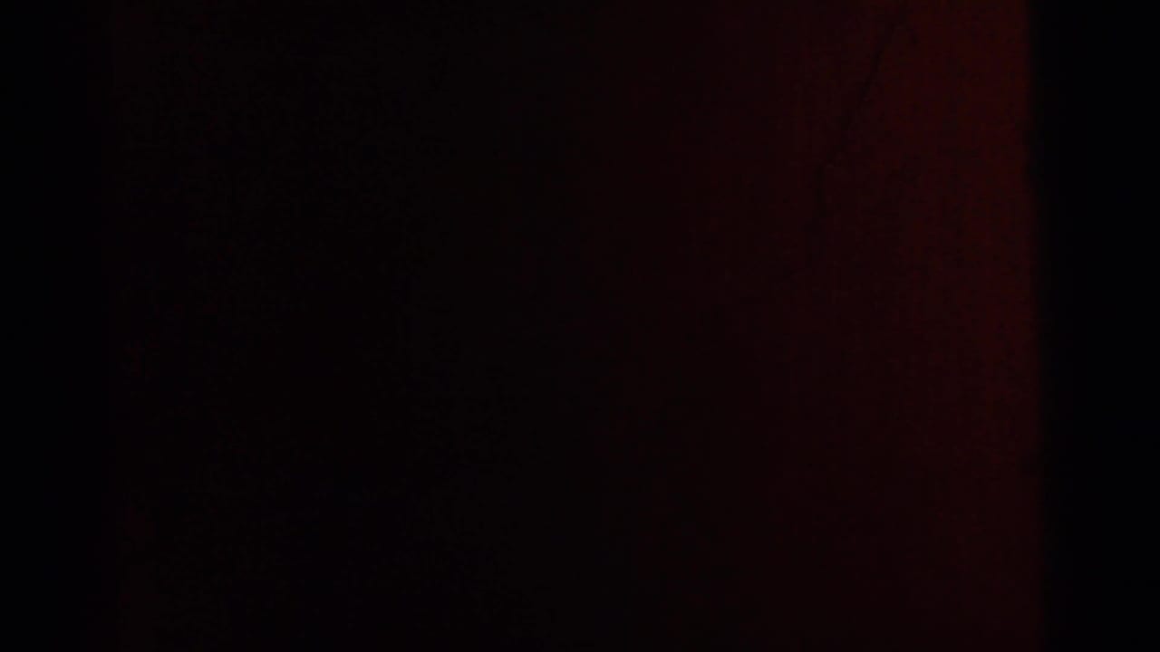 Nearly black interior frame with a reddish vertical band and faint film grain.