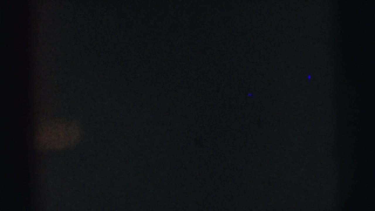 Dark frame with faint blue specks and a small pale patch near the center-left.