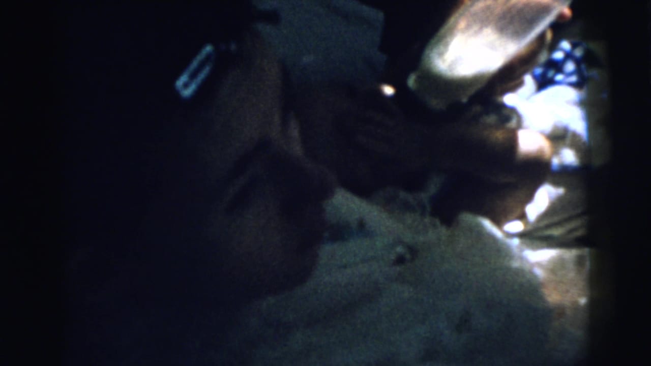Dim close-up of an infant being bottle-fed by an adult hand.