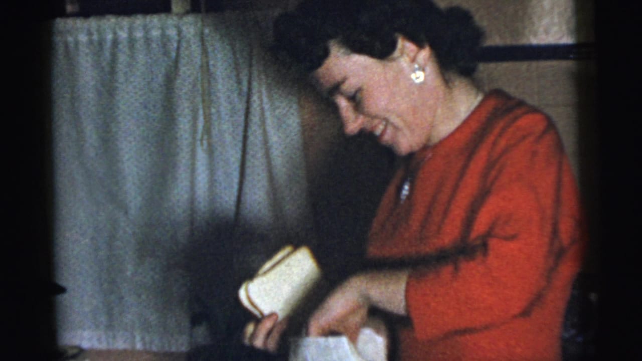 The woman in red looks down and handles a light-colored gift inside the Gary, Indiana home gathering.