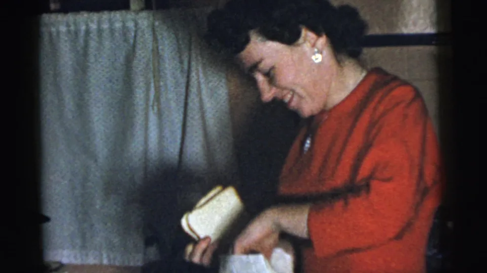 The woman in red looks down and handles a light-colored gift inside the Gary, Indiana home gathering.