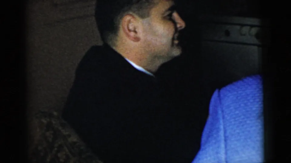 A man in a dark suit appears in profile beside a person in blue during the Gary, Indiana home gathering.