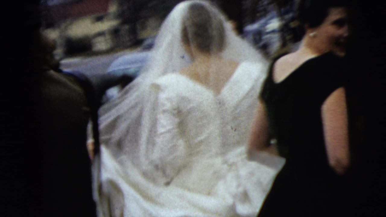 The bride's veil and gown fill the frame as attendants walk beside her on a Moline street in the supplied 1962 context.