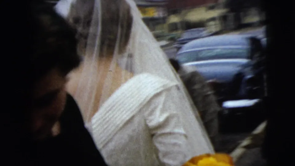 A close handheld view shows the bride's veiled head and white dress while an attendant passes close to the camera.