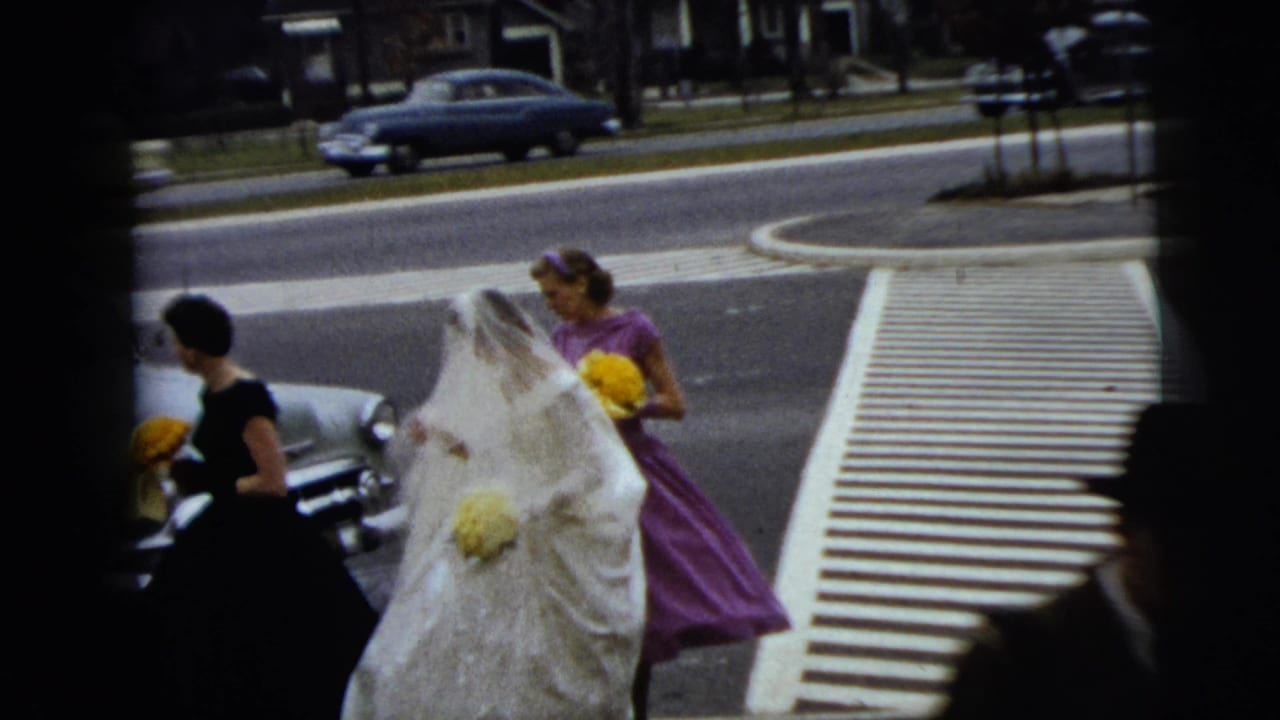 Bride and bridesmaids with yellow bouquets walk beside a crosswalk as cars pass behind them.