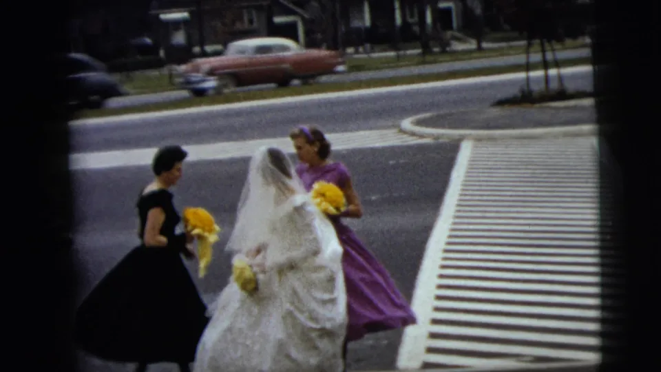 The bridal party remains near the crosswalk in Moline, with the bride's veil and yellow bouquets prominent against street traffic.