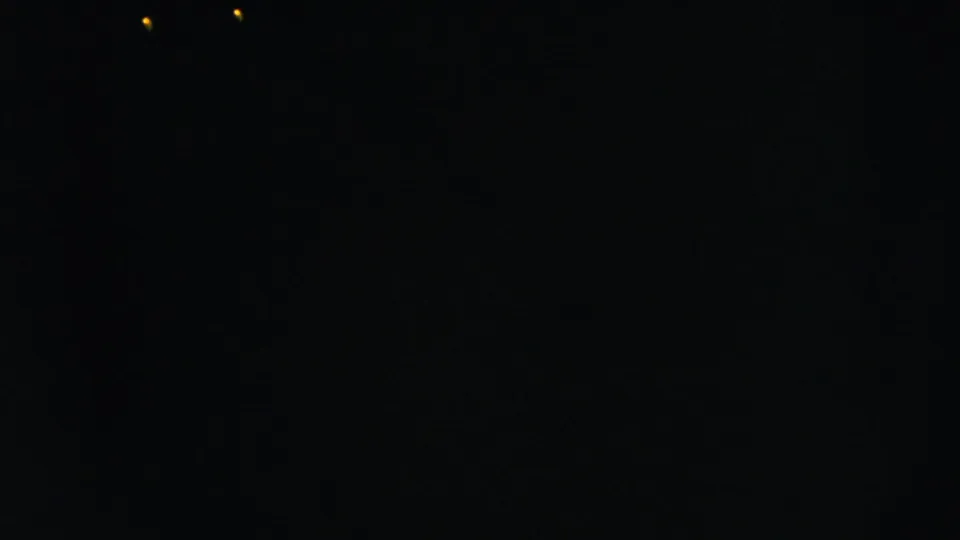 A largely dark 8mm frame, likely between visible moments, with minimal detail and small light points near the lower left.