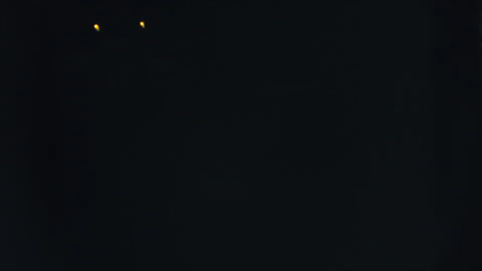 Dark 1962 8mm frame from Moline, Illinois showing two small yellow lights with faint film texture.