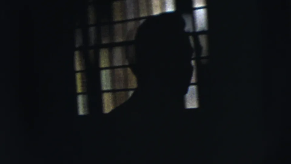 1962 Moline 8mm frame with a silhouetted figure crossing before a barred window inside a dark room.