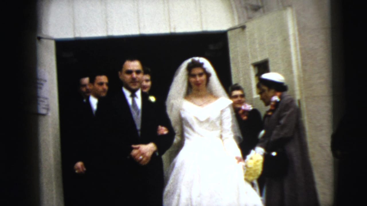 Bride and groom step out of a doorway while guests stand nearby.