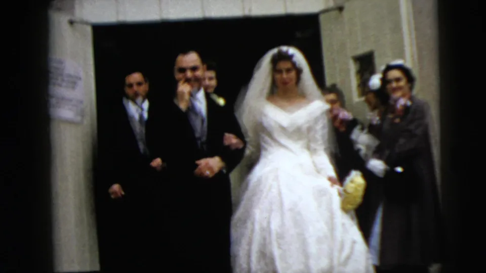 The bride and groom remain arm-in-arm near the building exit, surrounded by formally dressed guests in this 1962 Moline wedding scene.