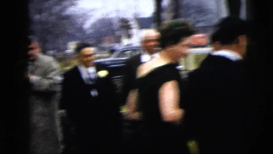 Guests in period formalwear move past the camera in a soft, handheld 8mm view of the wedding departure.
