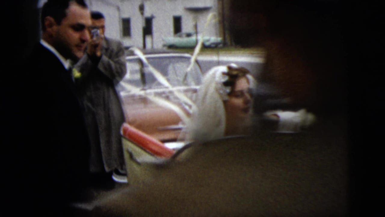 In 1962 Moline, Illinois, a bride in a white veil stands by a red-and-white convertible as suited men and a photographer gather nearby.