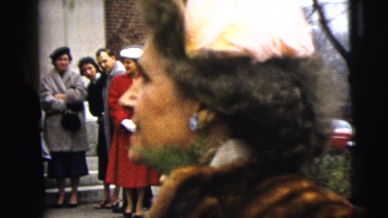 Woman in fur coat and pale hat passes in front of women standing near a building entrance.