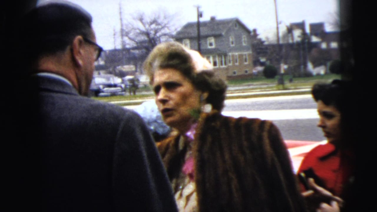 A 1962 Moline street scene shows a serious-looking woman in a fur coat facing a suited man while another woman in red stands at the edge.