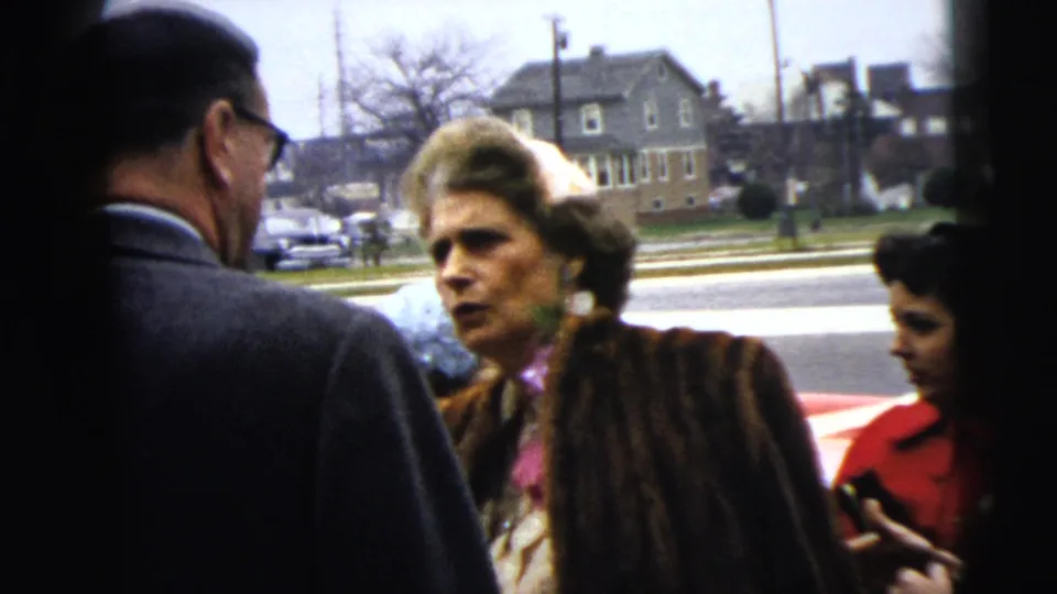 A 1962 Moline street scene shows a serious-looking woman in a fur coat facing a suited man while another woman in red stands at the edge.