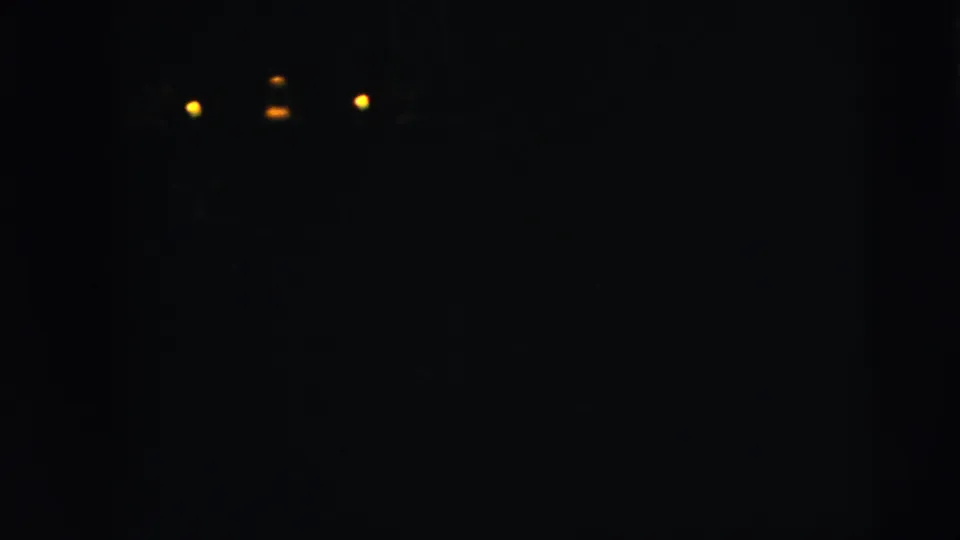 The scene shifts to a dark night view with several distant yellow lights visible in the upper part of the frame.