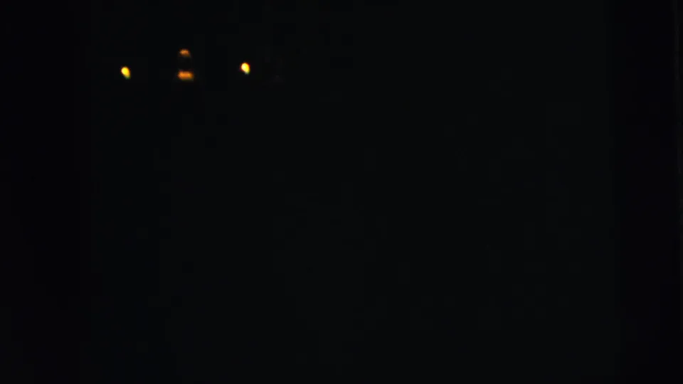 A dark 8mm night shot shows three distant glowing lights with little surrounding detail visible.