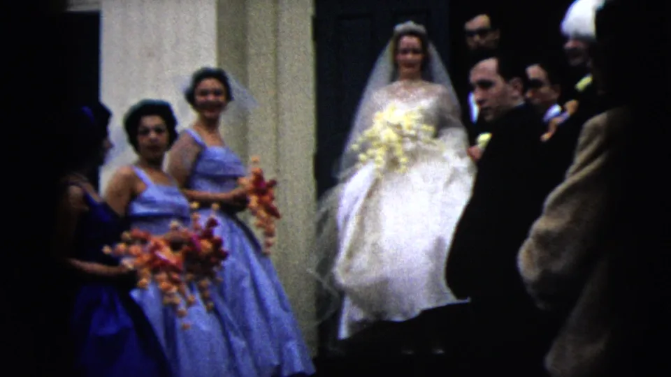 The bride and bridesmaids remain at the Moline church entrance while suited guests look on in 1962 8mm wedding footage.