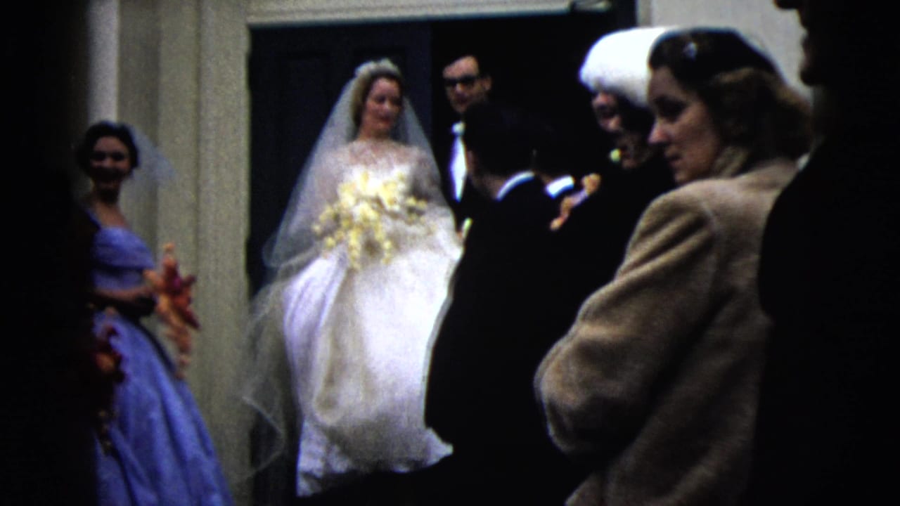 Bride in white stands at a doorway with bridesmaids and suited guests nearby.