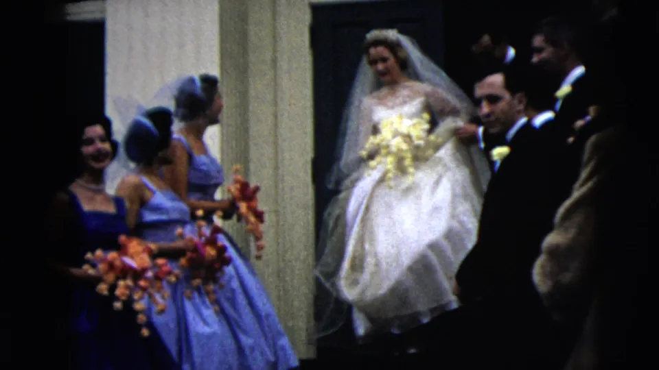 Bridesmaids in blue hold bright bouquets while the bride in white emerges from the doorway during the 1962 Moline wedding footage.