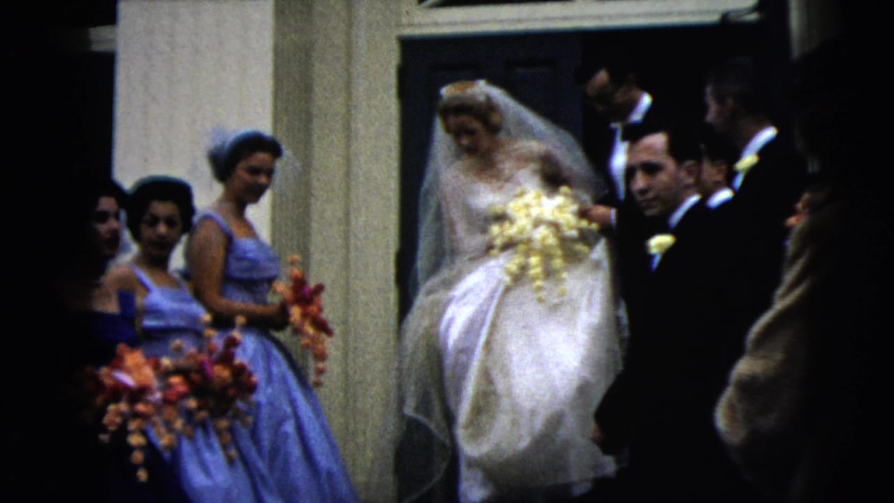 Bride in white gown exits a building with bridesmaids in blue dresses and men in dark suits.