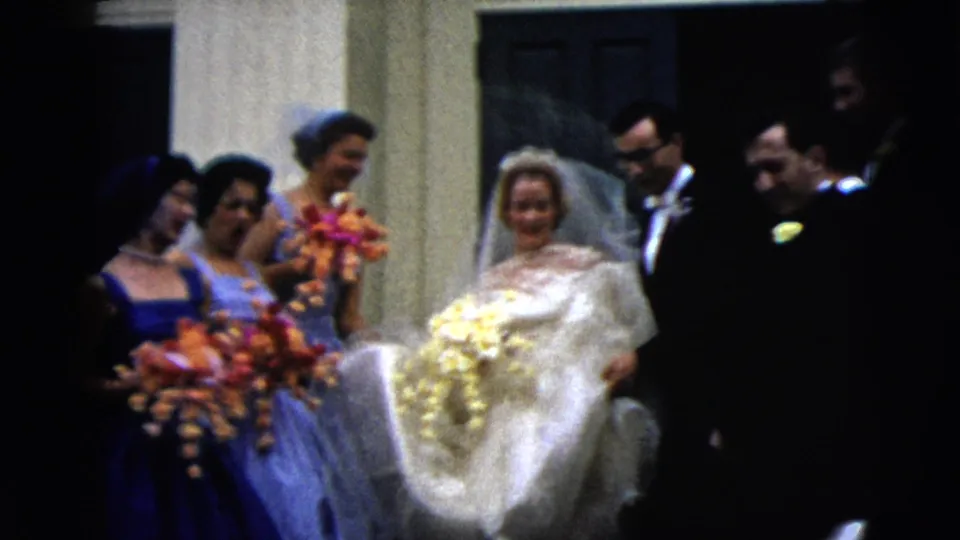 In Moline, Illinois in 1962, a bride in a white gown and veil stands with bridesmaids in blue dresses and men in tuxedos near a church doorway.