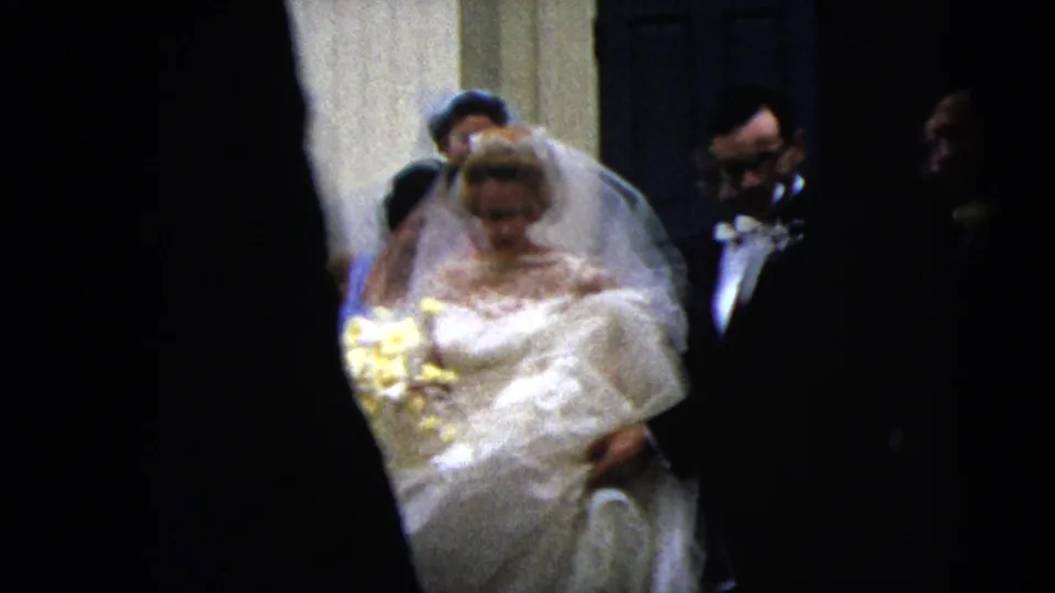 A bride in a white gown and veil walks forward with her bouquet while the groom and attendants follow behind in the 1962 Moline home movie.