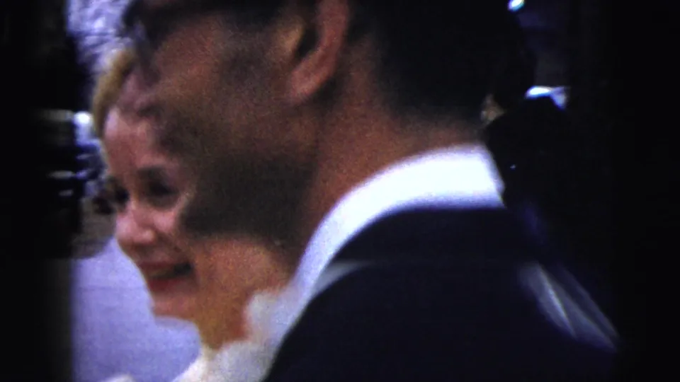 The bride smiles beside a man in a dark suit or tuxedo, with guests close around them in the 1962 Moline wedding scene.