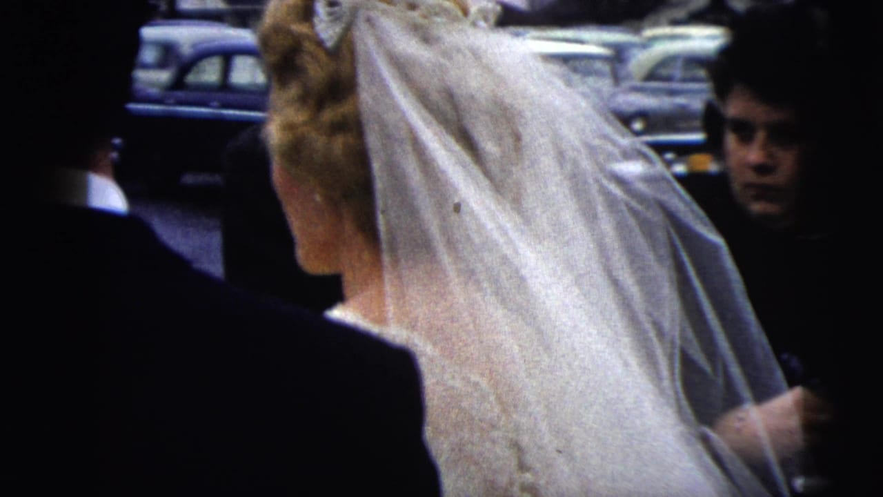 Bride in veil beside a groom or guest in a dark suit, with a young face at the right edge.