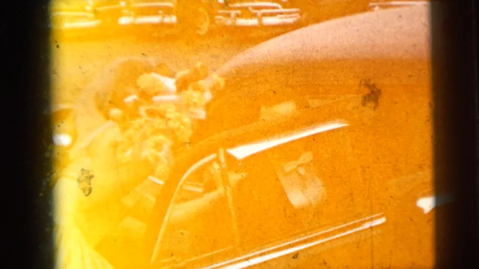 Yellow-orange 8mm frame showing the bride and groom at the black car during their 1962 Moline wedding departure.